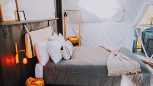 A cozy tent-style room with a bed, wooden floor, and a small stool with a pizza. - Fordyce Geodesic Dome at Starlight Haven Resort (Hot Springs)