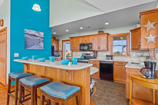A modern kitchen with wooden cabinets, a central island with stools, and a view of the outside through a window.
