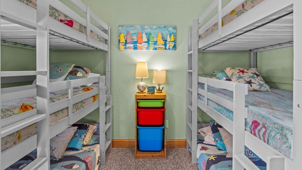 Camera con letto a castello, pareti verdi, un quadro con velieri e un tavolino con lampade e scatole portaoggetti.