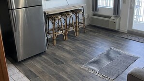 Cocina compacta con un refrigerador de acero inoxidable, una mesa de madera con cuatro sillas y un amplio ventanal con cortinas.