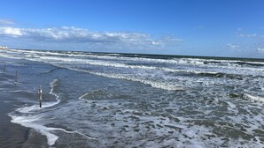 Una playa con olas, un muelle y cielo despejado.