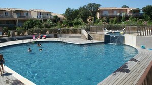 Ein Schwimmbad mit Holzterrasse, einer Wasserrutsche und Blick auf Wohnhäuser im Hintergrund.