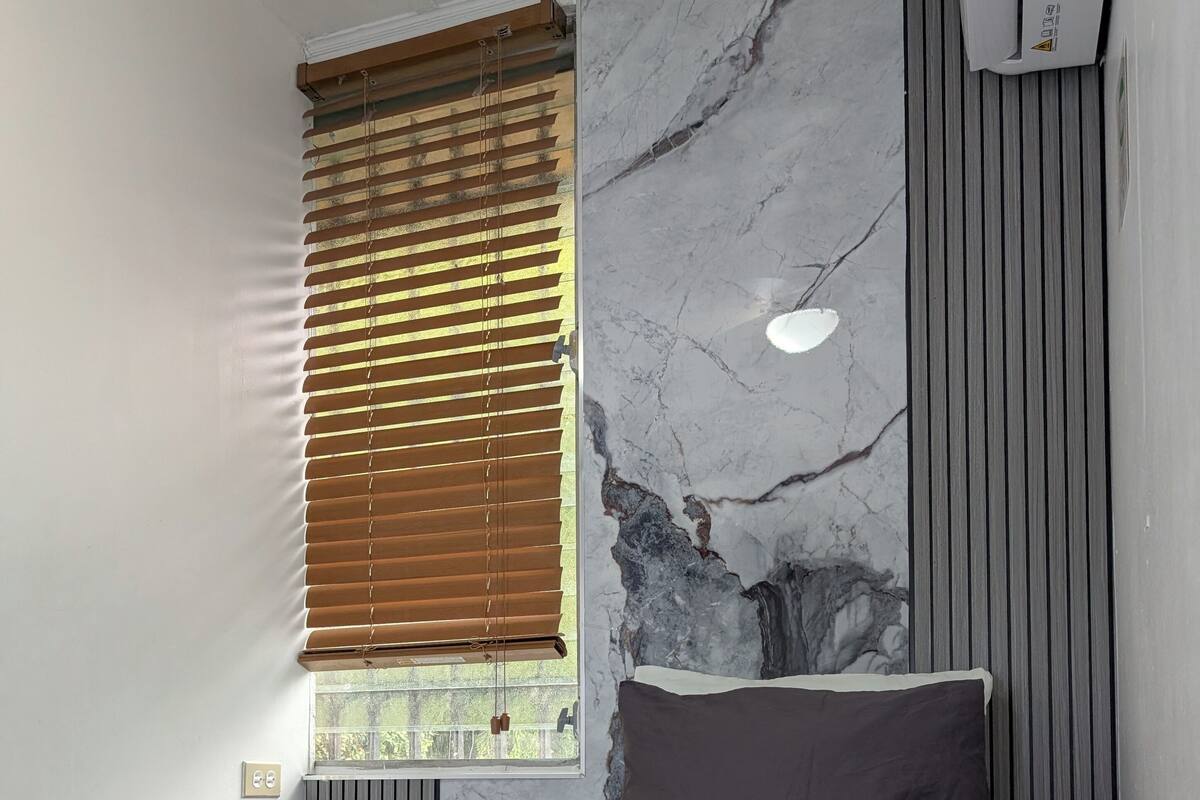 Quarto com cama, janela com persianas, radiador e parede de mármore.