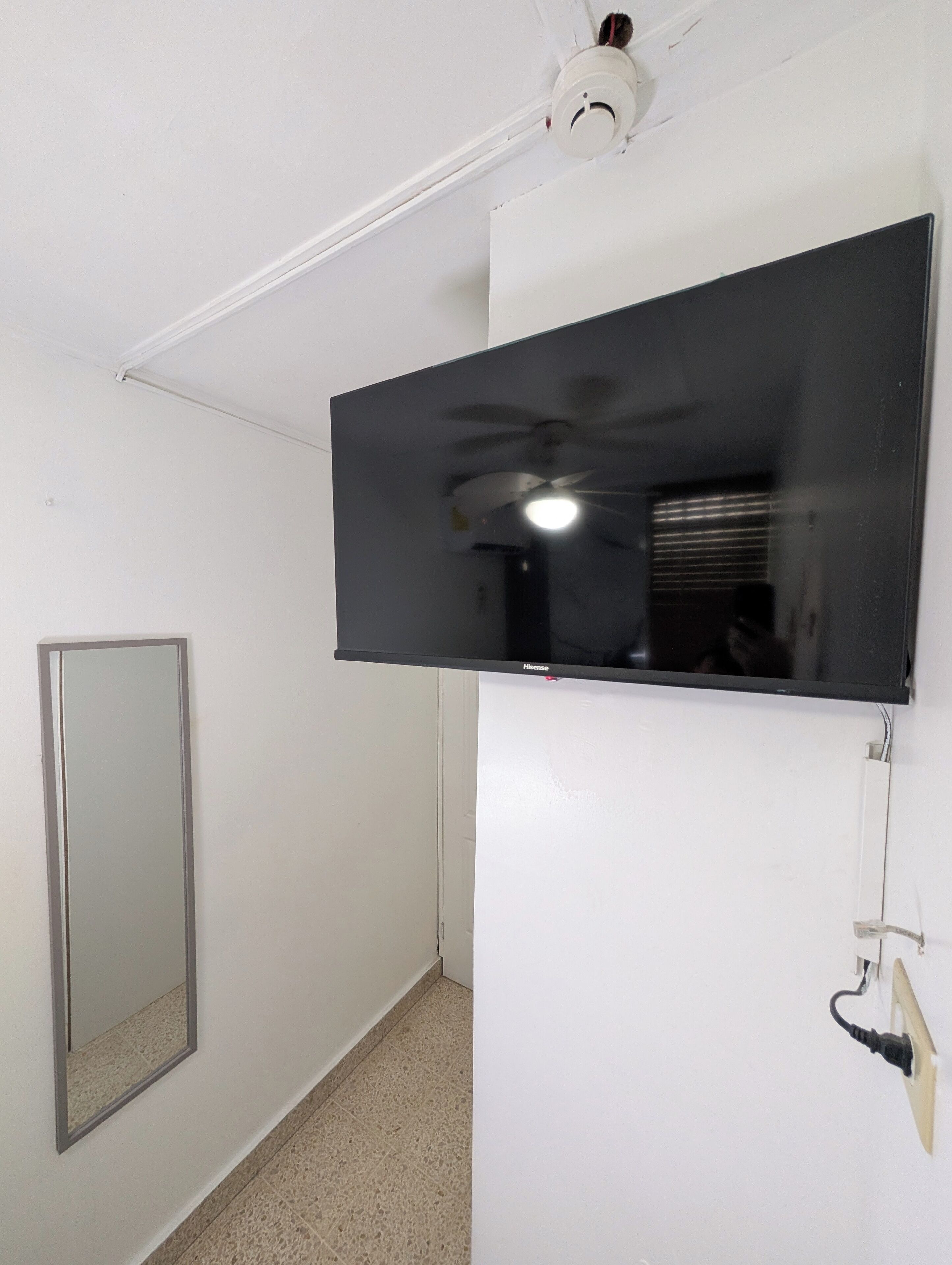 Una habitación con una televisión de pantalla plana montada, un ventilador de techo y una puerta.