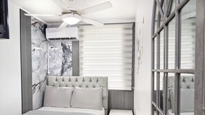 A modern bedroom with a tufted headboard, a bedside table with drawers, and a ceiling fan. - Hostal Yoha (Panama City)