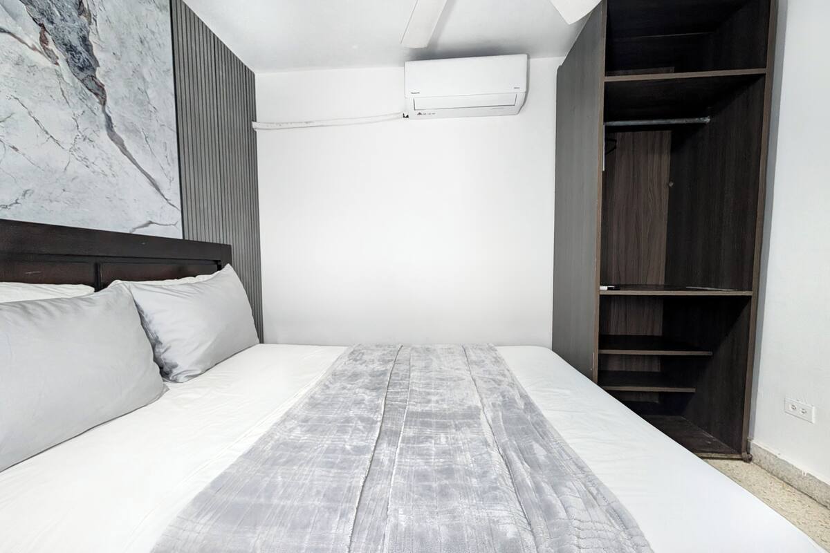 Quarto com cama, cabeceira, espelho grande, guarda-roupa e ar condicionado.