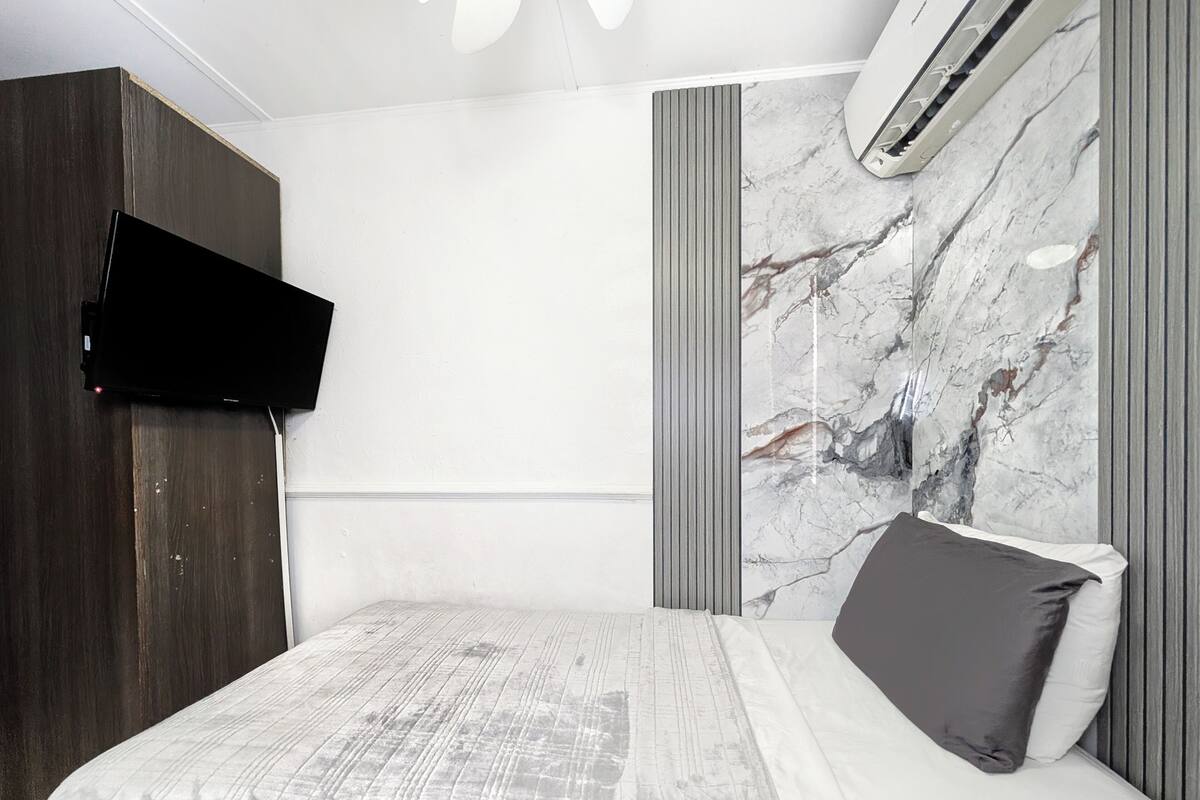 Quarto moderno com uma cama grande, televisão fixada na parede e revestimento de parede com padrão marmorizado.