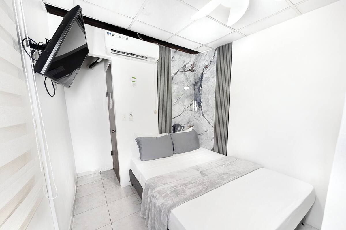 Quarto moderno com cama, TV de tela plana na parede e detalhes em parede com padrão marmorizado.