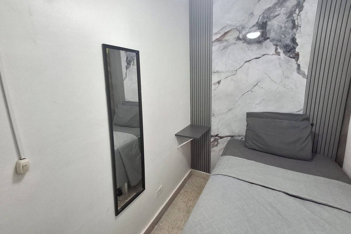 Quarto moderno com cama, mesa de cabeceira, espelho e parede com padrão marmorizado.