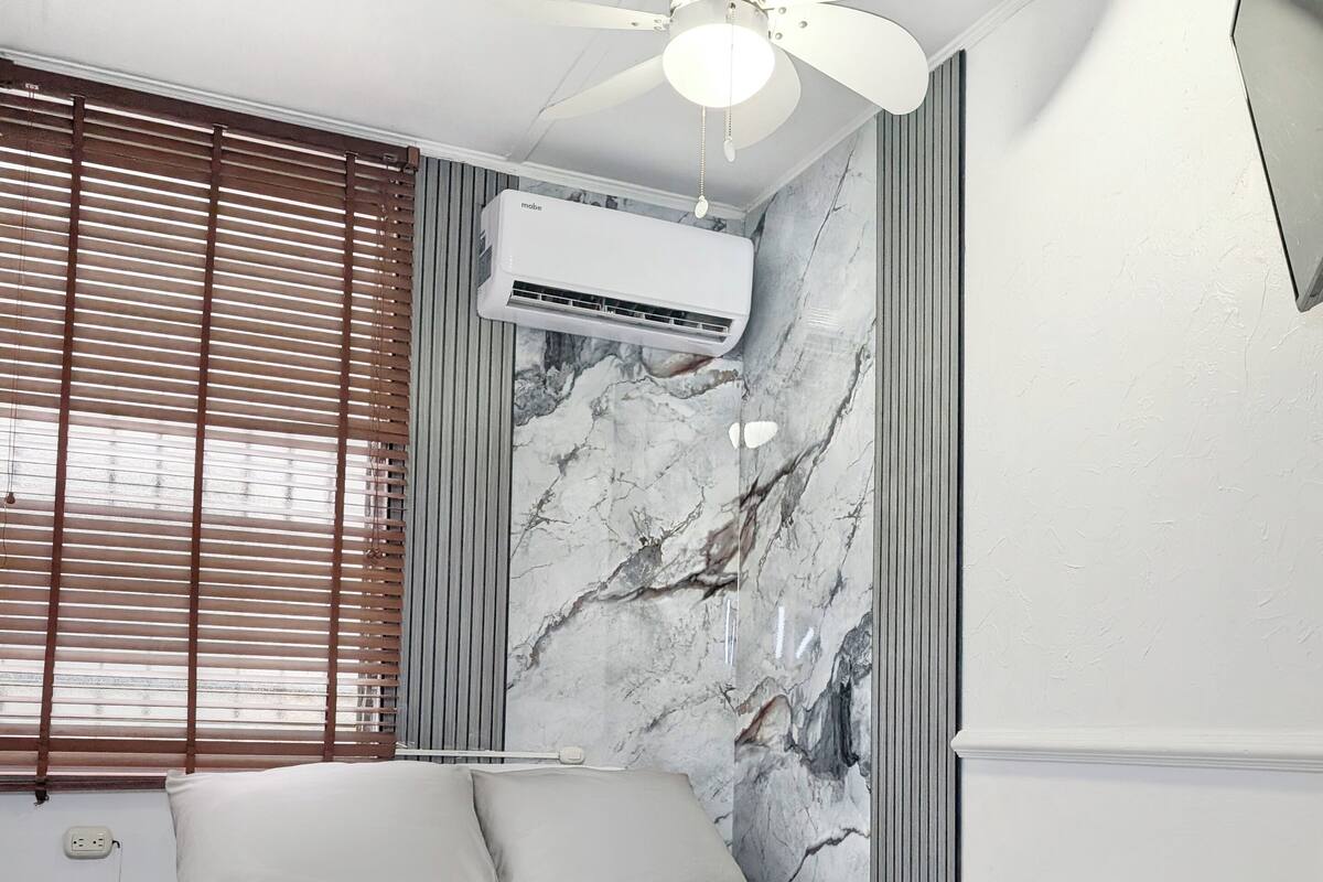 Quarto moderno com cama, ventilador de teto e parede com padrão marmorizado.