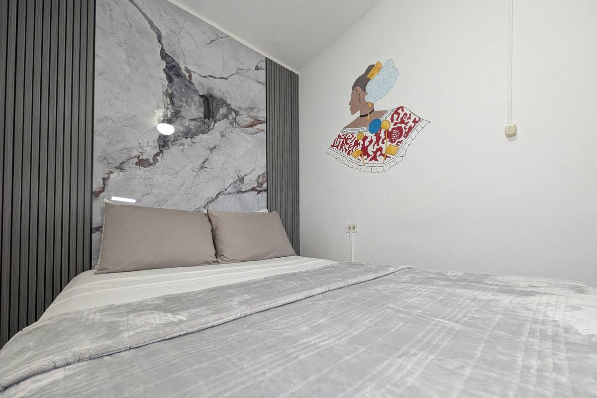 Quarto moderno com cabeceira estampada em mármore, cama com roupa de cama cinzenta e obra de arte na parede.