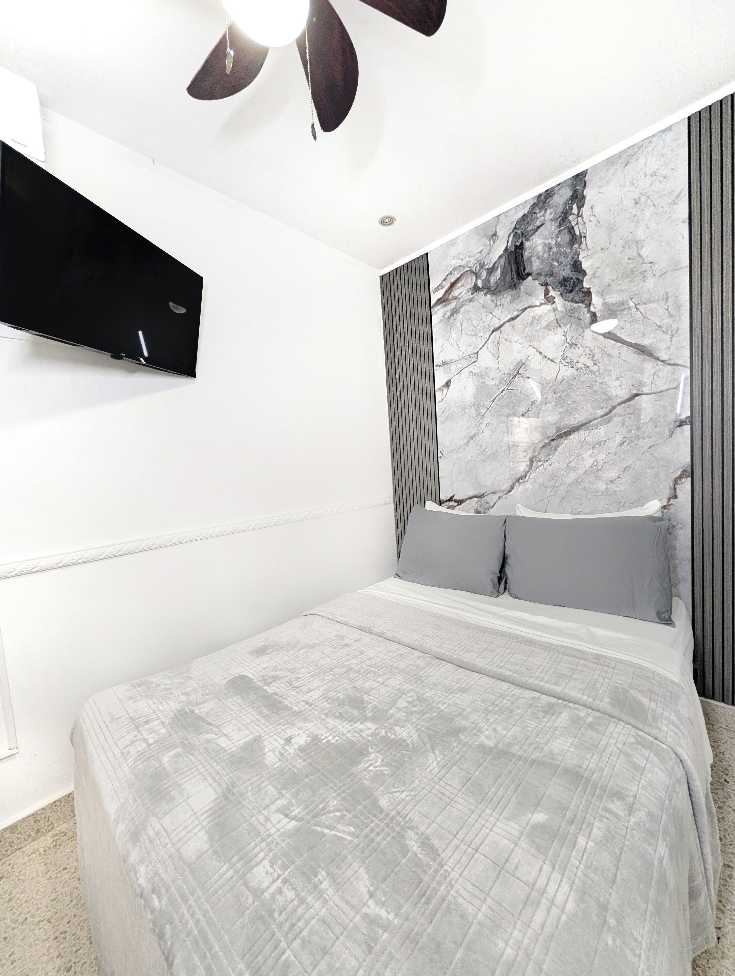 Une chambre moderne avec un lit, un téléviseur fixé au mur et un ventilateur de plafond.