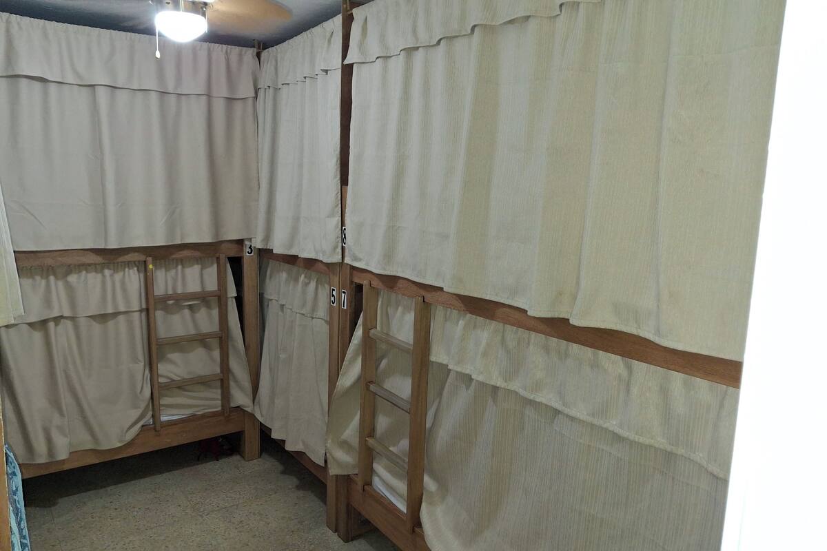Quarto com beliches, escadas de madeira e cortinas.
