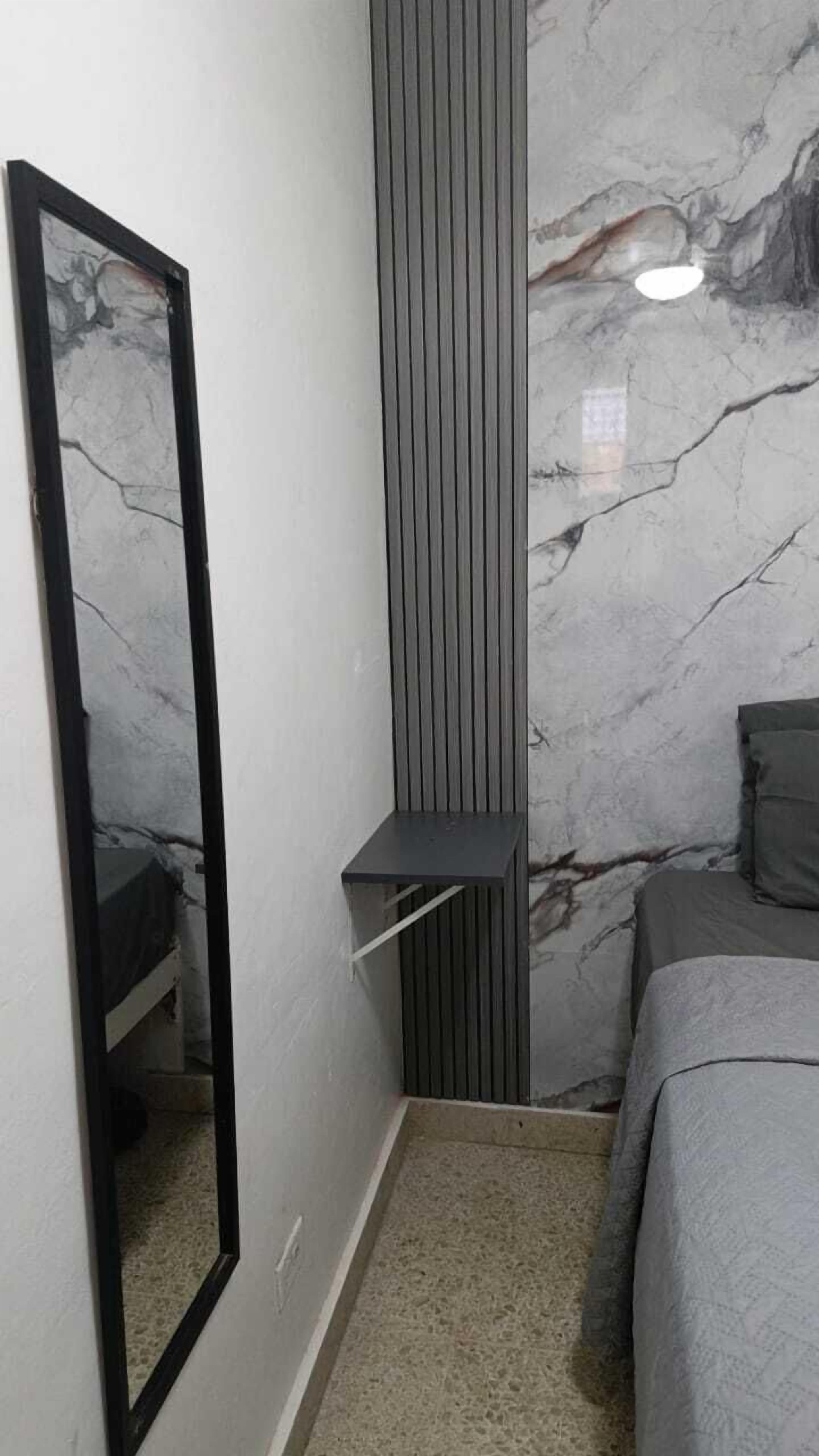 A bedroom with a bed, a bedside table, a mirror, and a wall with a marble pattern.