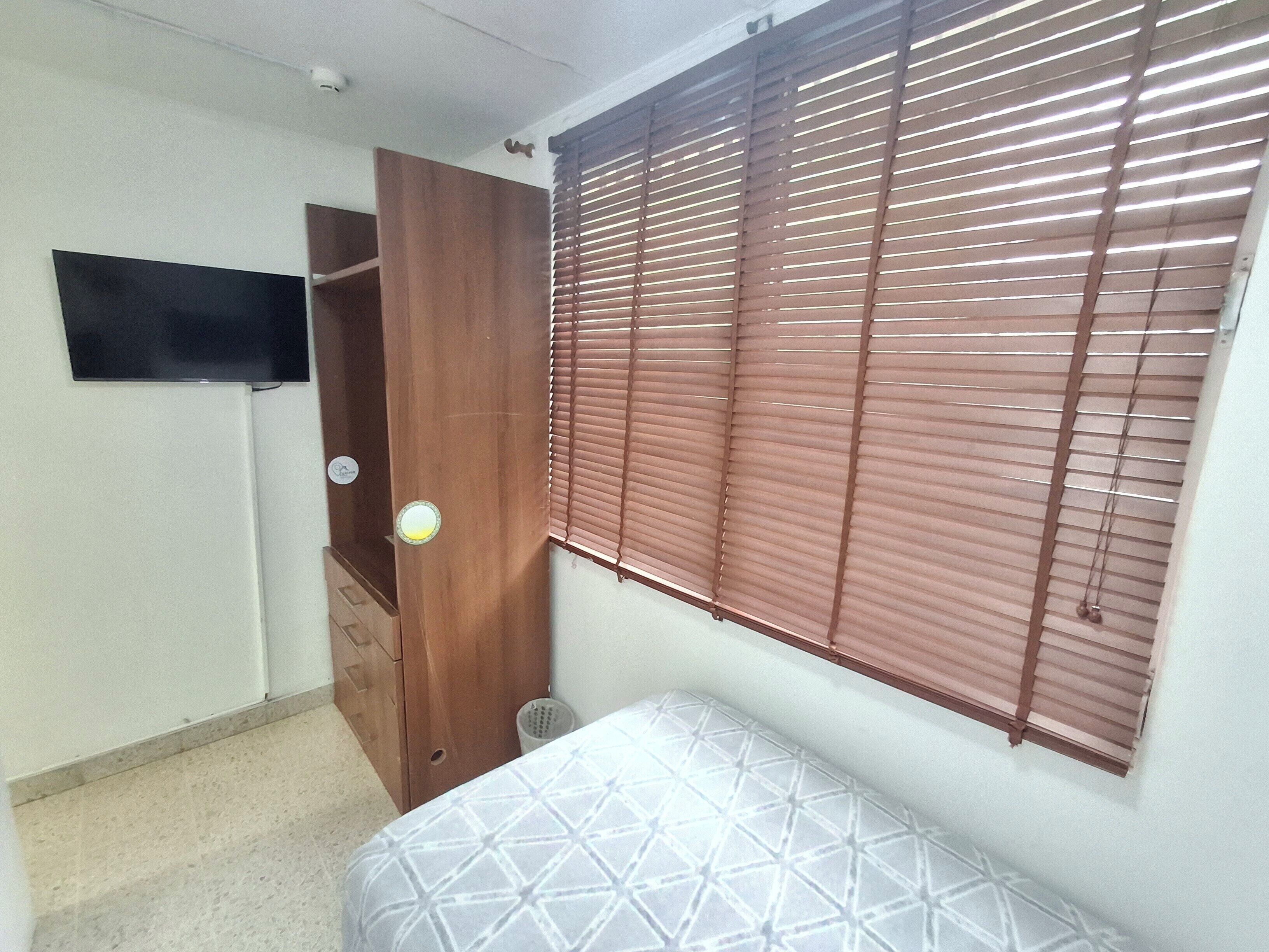 Un dormitorio con cama, armario de madera, televisor y ventana con persianas.