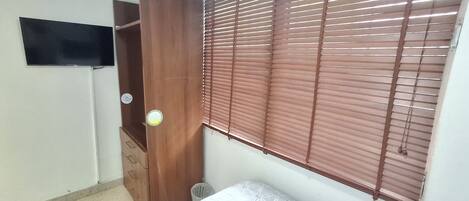 Un dormitorio con cama, armario de madera, televisor y ventana con persianas.
