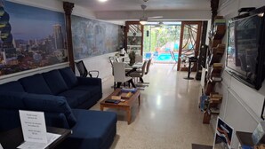 A hotel lobby with a large cityscape mural, a blue sofa, a coffee table with chess pieces, and a sign detailing towel rental and bath soap prices. - Hostal Yoha (Panama City)