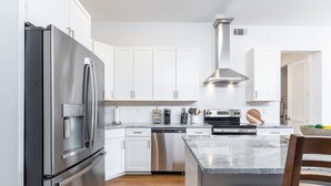 A modern kitchen with stainless steel appliances, white cabinetry, and a granite countertop. - East Nashville Luxury Condo~Rooftop Deck~Game Room~King Suite~Walk-In Showers (Nashville)