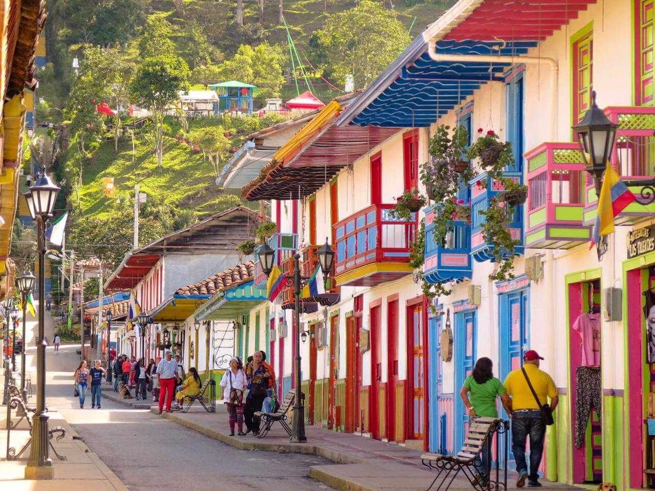 A colorful street with buildings, people walking, and hanging plants.