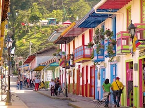 A colorful street with buildings, people walking, and hanging plants. - SAN PEDRO SALENTO APARTAHOTEL (Salento)