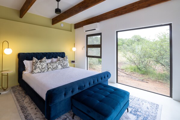 Een slaapkamer met een groot bed, een bankje, een bedlampje en uitzicht op het omliggende landschap.