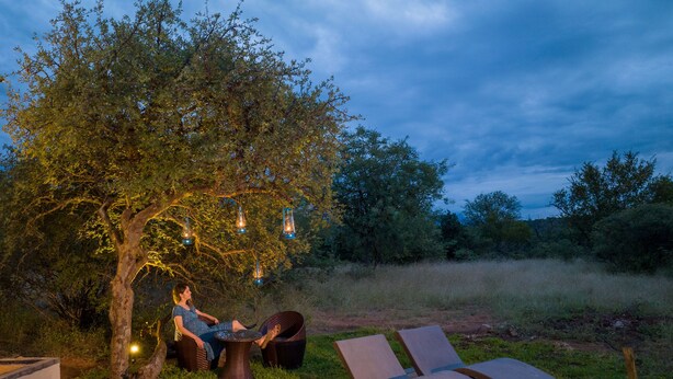 Un arbre décoré de lanternes suspendues, deux fauteuils et une petite table autour de laquelle sont assis deux personnes.