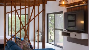 Un salon moderne avec un canapé bleu, un téléviseur fixé au mur et une grande fenêtre donnant sur l’extérieur.