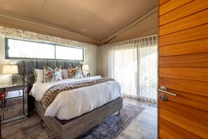 Une chambre à coucher avec un grand lit, une table de chevet, une porte en bois et une fenêtre avec des rideaux.