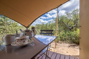 Une table avec une théière et des tasses, placée sous une tonnelle, d’où l’on peut admirer un paysage naturel.