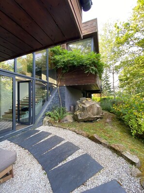 Una casa moderna con entrada de vidrio, un sendero de piedra y un jardín con rocas y plantas.
