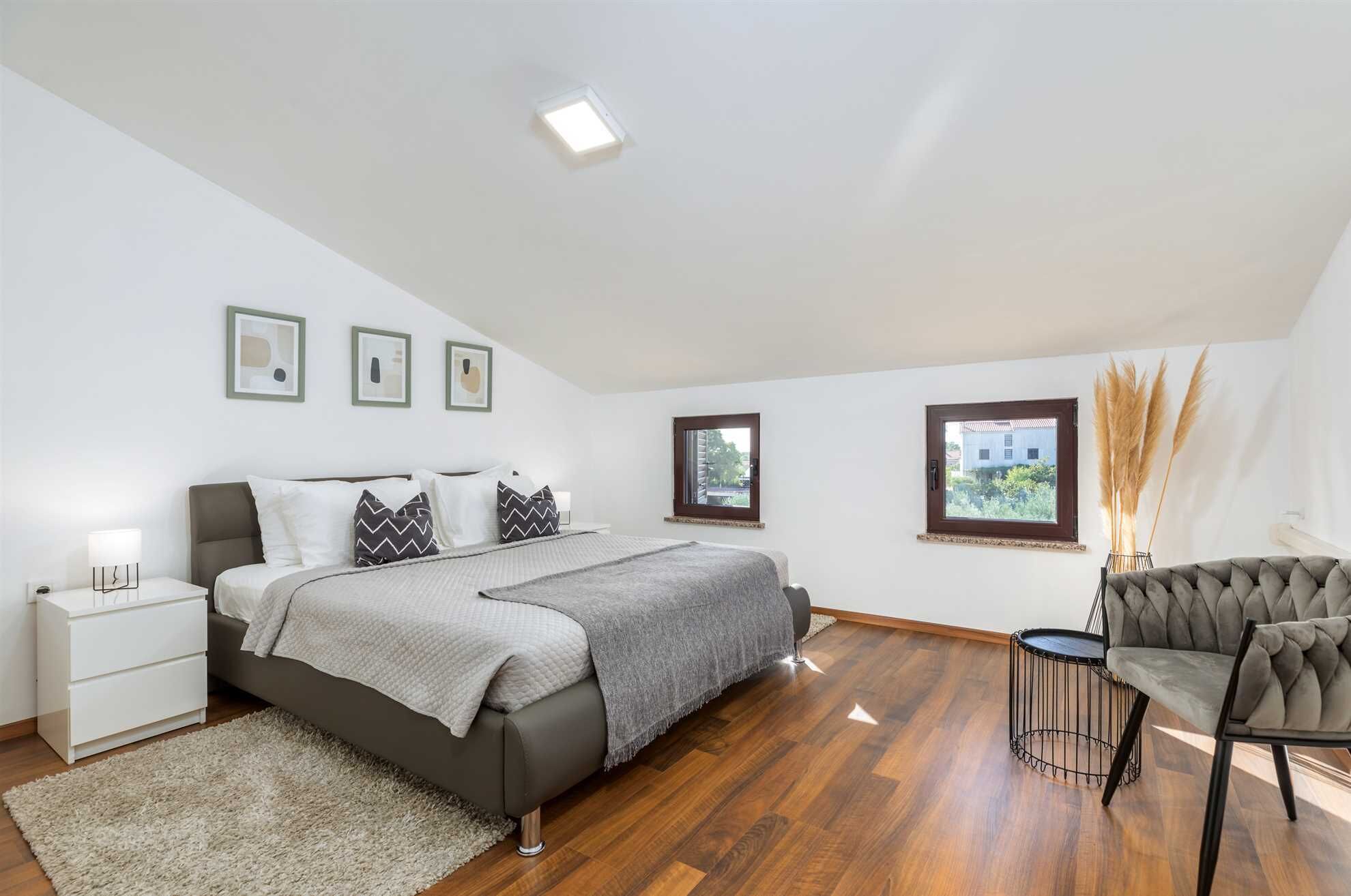 A bedroom with a bed, bedside tables, a chair, a window, and a view of the outside.