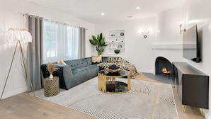 Ein modernes Wohnzimmer mit einem Ecksofa, einem Kamin und einem an der Wand befestigten Fernseher.