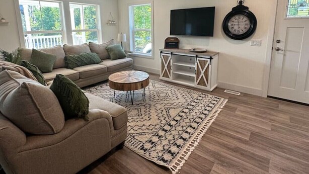 Una sala de estar con un sofá color beige, una mesita de centro, un tapete estampado y un televisor en la pared.