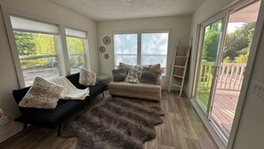 Un salón amplio con un sofá seccional negro y beige, una alfombra de pelo alto y ventanas grandes que ofrecen vistas al exterior.