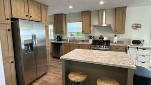 Una cocina moderna con armarios de madera, un refrigerador de acero inoxidable, una isla central con taburetes y un microondas.