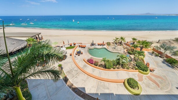 Un complexe hôtelier de bord de mer doté d’une piscine, de chaises longues et de palmiers.