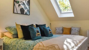 Une chambre avec un plafond en pente, un puits de lumière, un lit avec une literie à motifs et une œuvre d’art accrochée au mur.