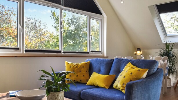 Un salon moderne avec un canapé bleu, des coussins jaunes, un bol blanc et une plante en pot sur une table basse en bois.