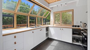 Eine moderne Küche mit großen Fenstern, weißen Schränken und einer Holzbalkendecke.
