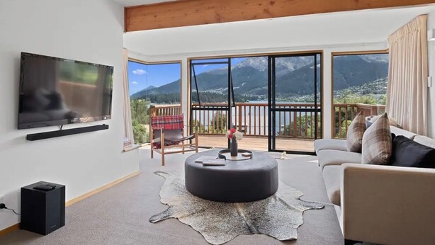 Ein geräumiges Wohnzimmer mit einem großen Flachbildfernseher, einem bequemen Sofa und einem runden Hocker.