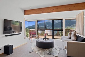 A spacious living room with a large flat-screen TV, a comfortable sofa, and a round ottoman.