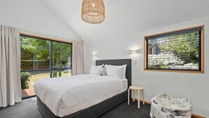 Ein modernes Schlafzimmer mit einem großen Bett, einem kleinen Hocker, einer einzigartigen Steinbank und einem großen Fenster mit Blick auf Grünflächen.