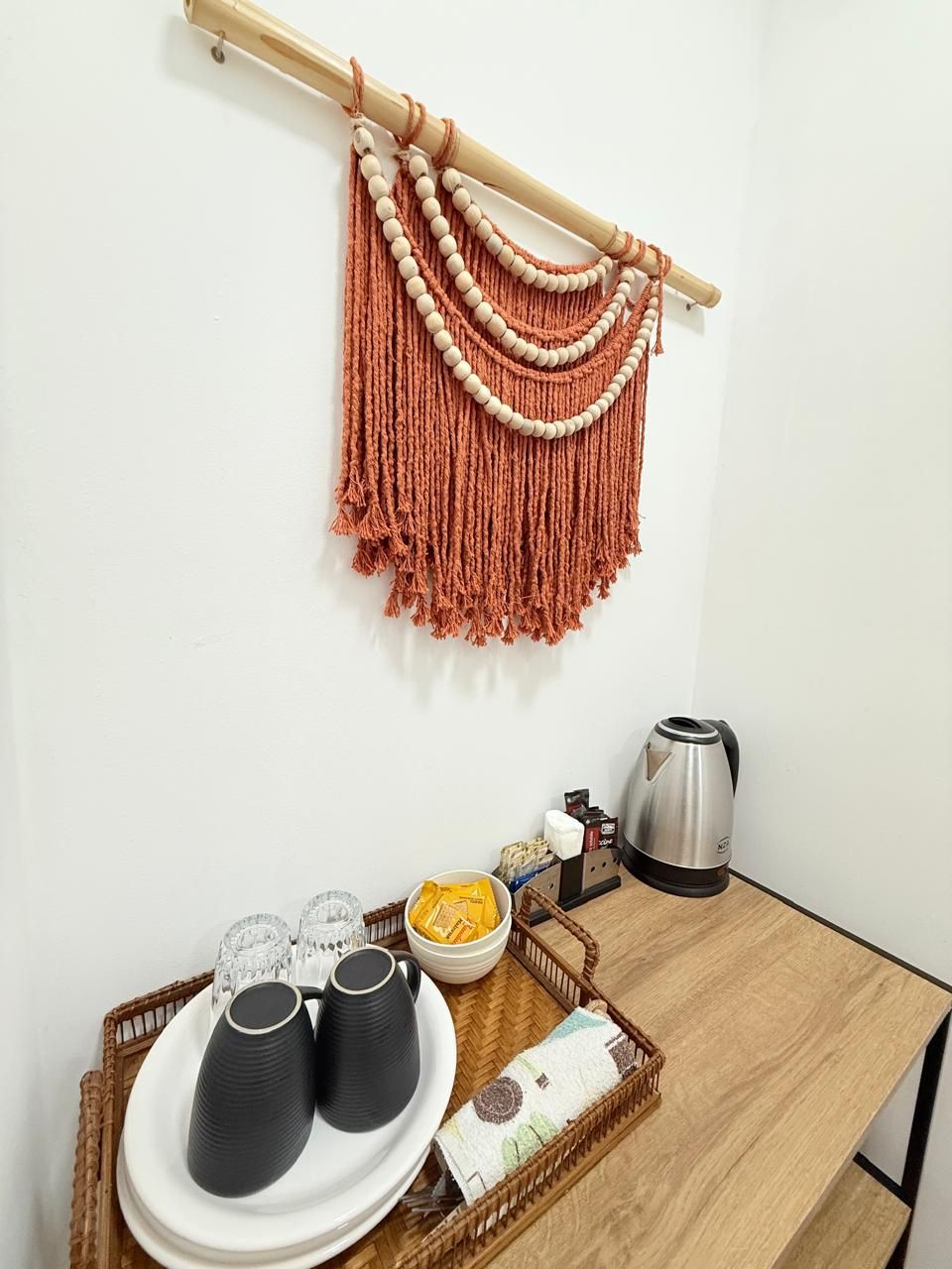 A kitchen area with a macrame wall hanging, a coffee maker, and a tray with cups and condiments.