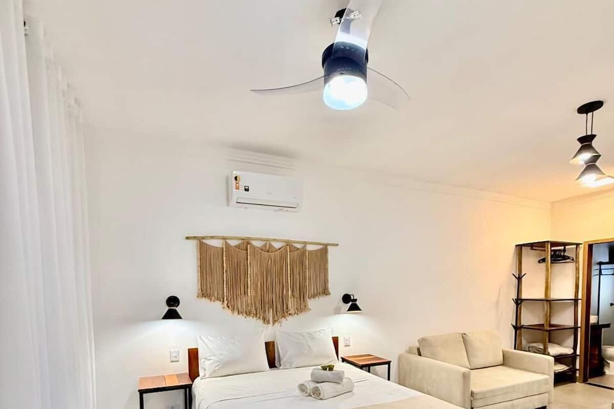 A hotel room with a large bed, two bedside tables, a sofa, and a ceiling fan.