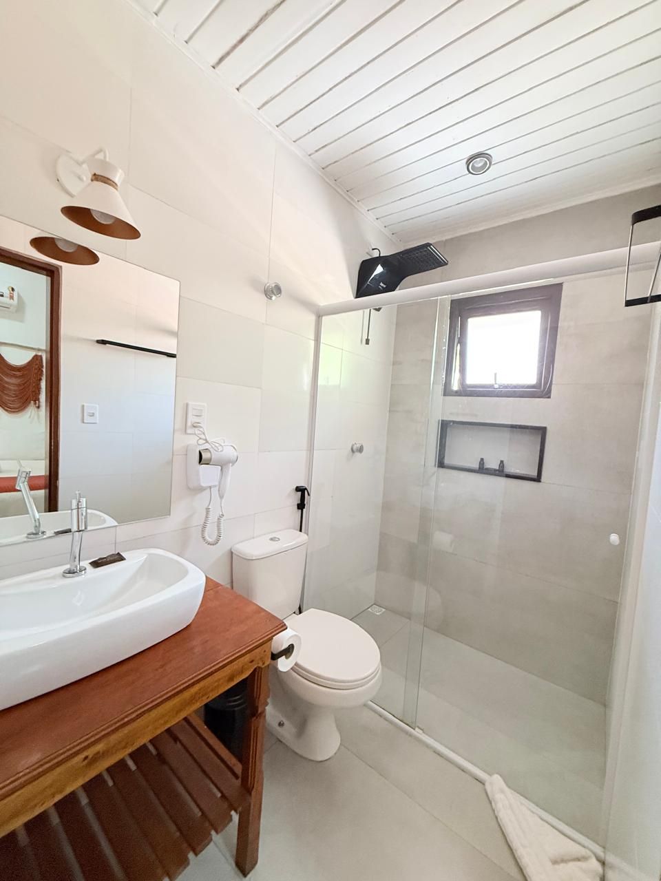 A modern bathroom with a wooden vanity, a white sink, a toilet, and a glass-enclosed shower area.