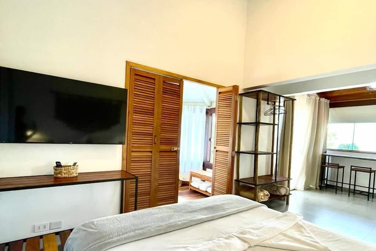 A hotel room with a bed, a TV, a wooden wardrobe, and a balcony with a table and chairs.