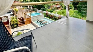 Et overdækket område udendørs med swimmingpool, liggestole og udsigt over et frodigt landskab.