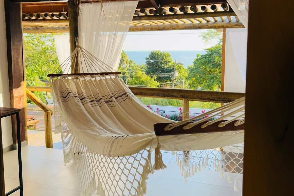 A hammock chair with a netted bottom, wooden ceiling, and a view of greenery outside.