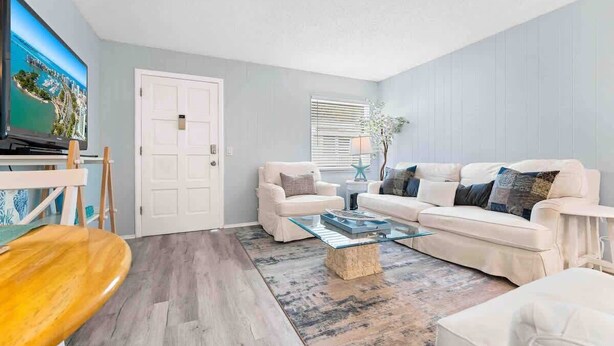 Ein Wohnzimmer mit Fernseher, zwei weißen Sofas, einem Glastisch und einem Holzstuhl.