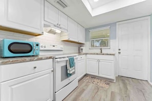A kitchen with white cabinetry, a blue microwave, a stove, and a window with blinds.